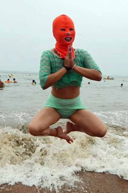 A swimmer wearing a hood known as facekini plays on the beach in Qingdao, east China's Shandong province, China, 16 July 2015. (Photo by Wang Haibin/EPA)