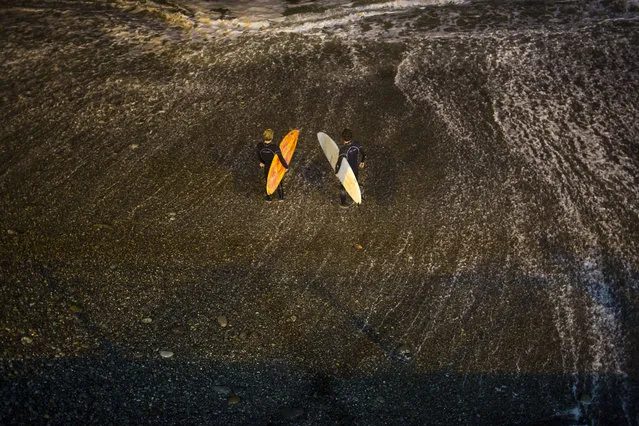 In this March 1, 2017 photo, surfers prepare to jump in the Pacific Ocean in La Pampilla beach in Lima, Peru. The Andean country has decked out Pampilla with four 1,000-watt lights like those used in soccer stadiums. Placed high above the beach, their lights reach about 200 meters out to the water, providing enough illumination to surf after nightfall. (Photo by Rodrigo Abd/AP Photo)