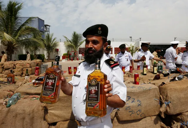 An officer from the Pakistan Maritime Security Agency (PMSA) holds liquor bottles for cameramen (unseen) while confiscated liquor bottles are displayed during a news conference in Karachi, Pakistan, May 4, 2016. According to PMSA, at least 12,400 bottles and cans of illegal liquor worth 60 million Pakistani Rupees were loaded on a boat that was intercepted at the open sea. (Photo by Akhtar Soomro/Reuters)