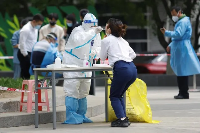 A medical worker wearing protective suit takes swab sample of a woman at a makeshift testing site following the coronavirus disease (COVID-19) outbreak in Beijing, China on April 25, 2022. (Photo by Carlos Garcia Rawlins/Reuters)
