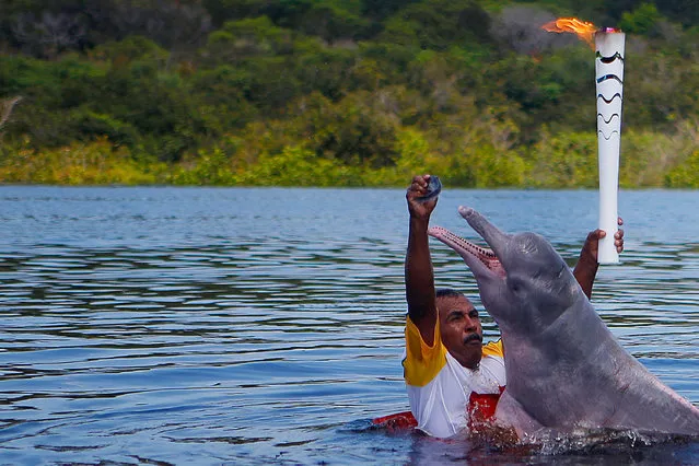 Resident Davi Souza gives a fish to a “Boto Cor-de-Rosa” (Pink River Dolphin), as he takes part in the Olympic Flame torch relay at Solimoes River in Iranduba city, Amazonas state, Brazil, June 20, 2016. (Photo by Fernando Soutello/Reuters/Courtesy of Rio2016)