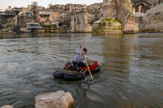 A boy tries to go against flow as he goes for fishing on the Tigris river with the abandoned old city of Hasankeyf in background on December 17, 2019. Despite years of protests by residents and activists, the small village on the banks of the Tigris River will soon be under water as part of a controversial dam project. Authorities have started to move some historic monuments, and have already destroyed others. Old city has been abandoned, government cut electricity and water, the historic market, has been destroyed and disappear during last days. Residents are being moved from the ancient town to a “New Hasankeyf” nearby, while historic artefacts have also been transported out of the area. (Photo by Bülent Kılıç/AFP Photo)