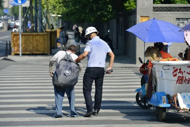 A beggar who lay at the side of a road pretending he had no legs was moved on by police who made him stand up and walk away. The man lay slumped on his front in Chengdu, in Sichuan Province, China, with his legs tucked under him, and his jeans stretched out to make it appear he had no legs. He is approached by a police officer, who bends down and talks to him for some moments. (Photo by Rex Features)