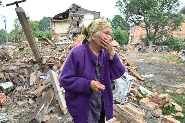 A local resident, Raisa Kuval, 82, reacts next to a damaged building partially destroyed after a shelling in the city of Chuguiv, east of Kharkiv, on July 16, 2022. In the northeast region around Ukraine's second city of Kharkiv, governor Oleg Synegubov said an overnight Russian missile attack killed three people in the town of Chuguiv. (Photo by Sergey Bobok/AFP Photo)