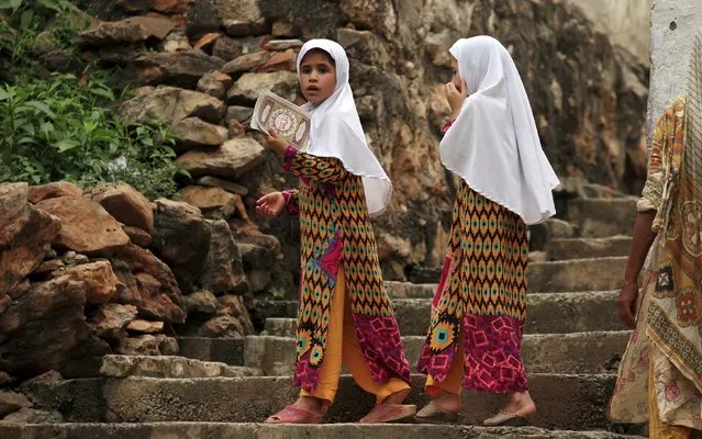 A girl holds a book containing short verses from the Koran while standing with her sister outside their home at a historic site at Saidpur village on the outskirts of Islamabad, Pakistan August 20, 2015. (Photo by Faisal Mahmood/Reuters)