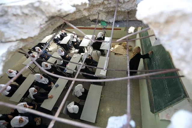 Palestinian schoolgirls, pictured through a hole in the roof of a classroom that witnesses said was damaged by Israeli shelling during a 50-day war last summer, attend a lesson on the first day of a new school year at Suhada Khouza school in Khan Younis in the southern Gaza Strip August 24, 2015. (Photo by Ibraheem Abu Mustafa/Reuters)