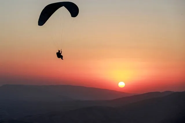 A member of the Sulaymaniyah paragliding team glides by the setting sun after a launch from Mount Azmar over Iraq's northeastern city of Sulaymaniyah in the autonomous Kurdistan region on July 1, 2022. (Photo by Ahmad Al-Rubaye/AFP Photo)