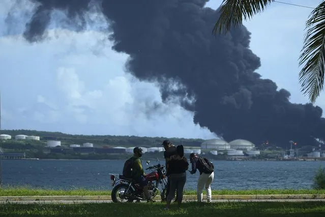People watch a huge rising plume of smoke from the Matanzas Supertanker Base, as firefighters try to quell a blaze which began during a thunderstorm the night before, in Matazanas, Cuba, Saturday, August 6, 2022. Cuban authorities say lightning struck a crude oil storage tank at the base, causing a fire that led to four explosions which injured more than 50 people. (Photo by Ramon Espinosa/AP Photo)