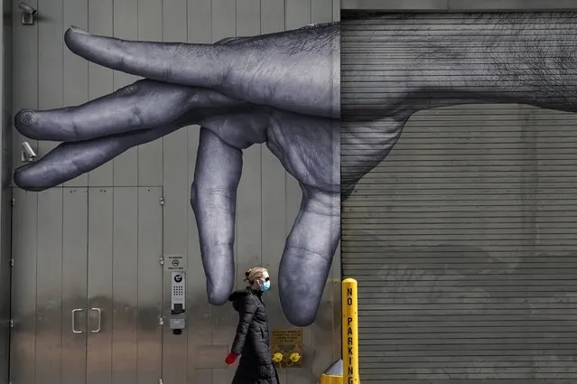 A woman in a mask walks past a mural of a hand on the side of a building in Midtown New York City on April 22, 2020. Governor Andrew M. Cuomo said he would extend New York State's shutdown until May 15 in coordination with other states to make progress in containing the coronavirus. (Photo by Timothy A. Clary/AFP Photo)