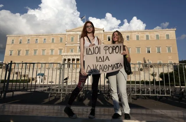 A lesbian couple Christina, left, and Ioanna hold a banner that reads “Same taxes, same rights” during a protest outside Greece's Parliament in Athens on Friday, September 5, 2014. Several hundred people took part in the peaceful march to Parliament, which is debating draft legislation to outlaw Holocaust denial and expand prosecution powers against the incitement of racial violence. (Photo by Thanassis Stavrakis/AP Photo)