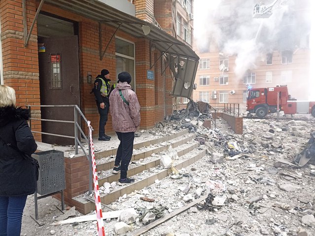 People and a Ukrainian serviceman watch as firefighters work to extinguish a fire at a damaged apartment building after a Russian attack in Odesa, Ukraine, Friday, December 29, 2023. (Photo by Artem Perfilov/AP Photo)