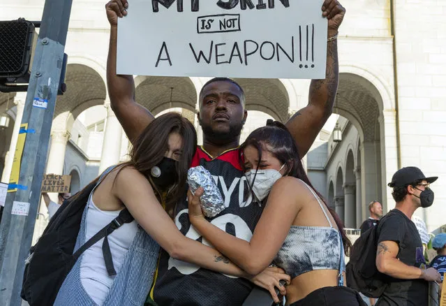 Couture designer Jared Lamar holds up a sign and is hugged by fellow protesters Shea Vasquez, left, and Carly Trabilcy during a demonstration Saturday, June 6, 2020, outside Los Angeles City Hall, sparked by the death of George Floyd, who died May 25 after he was restrained by Minneapolis police. The sign reads: “The color of my skin is not a weapon!!!”. (Photo by Damian Dovarganes/AP Photo)