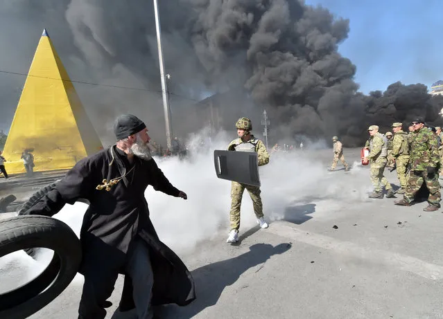 An Orthodox priest throws a tyre as Maidan self-defence activists clash with fighters of Kiev-1 volunteer battalion on Independence Square in Kiev on August 7, 2014. Kiev's municipal services protected with the servicemen tried to remove tents from the city's central Independence Square, also known as Maidan, and free Khreshchatyk Street for the traffic. Some few hundreds of Maidan activists still live in the tent camp set in the center of the Ukrainian capital that upsets the vast majority of the local residents. (Photo by Sergei Supinsky/AFP Photo)