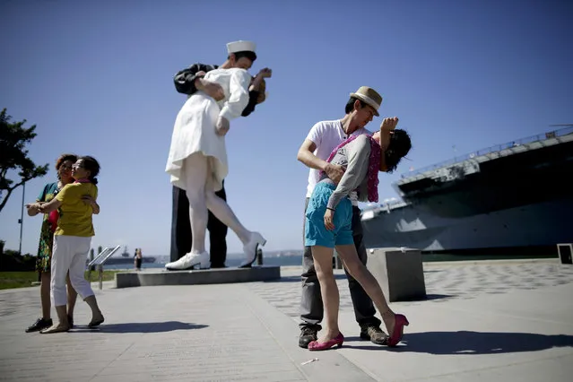 Jie Quan, second from right, of China, dips Juan Wang, also of China, as they pose for family members in front of the sculpture “Unconditional Surrender”, Friday, September 18, 2015, in San Diego. The sculpture by Seward Johnson is inspired by Alfred Eisenstaedt's iconic photo of a sailor kissing a nurse in Times Square on V-J Day. (Photo by Gregory Bull/AP Photo)