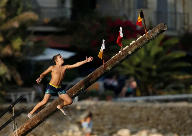 A child tries to grab a flag on the “gostra”, a pole covered in grease, during the religious feast of St Julian, patron of the town of St Julian's, outside Valletta, Malta, August 27, 2016. In the traditional “gostra”, a game stretching back to the Middle Ages, young men, women and children have to make their way to the top and try to uproot one of the flags to win prizes. From May to September in Malta, there is hardly any weekend when a town or a village is not celebrating the feast of its patron saint or other saints revered in different churches. (Photo by Darrin Zammit Lupi/Reuters)