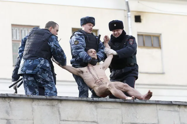 Interior Ministry members detain artist Pyotr Pavlensky after he cut off a part of his earlobe while sitting on the wall enclosing the Serbsky State Scientific Center for Social and Forensic Psychiatry during his protest action titled “Segregation” in Moscow October 19, 2014. (Photo by Maxim Zmeyev/Reuters)