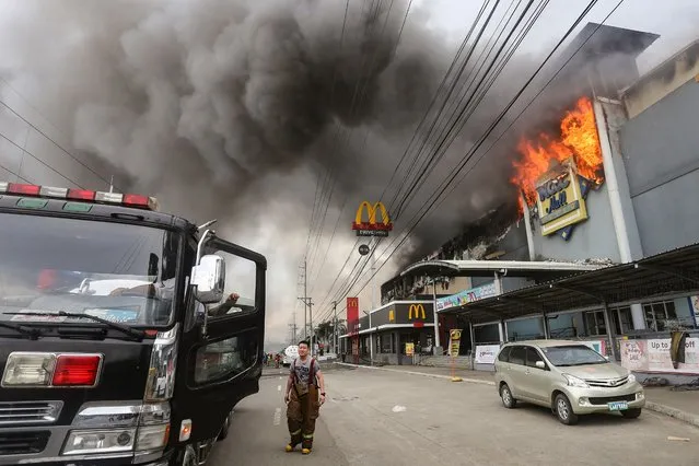 This photo taken on December 23, 2017 shows a firefighter standing in front of a burning shopping mall in Davao City on the southern Philippine island of Mindanao. Thirty-seven people were believed killed in a fire that engulfed a shopping mall in the southern Philippine city of Davao, local authorities said on December 24. (Photo by Manman Dejeto/AFP Photo)
