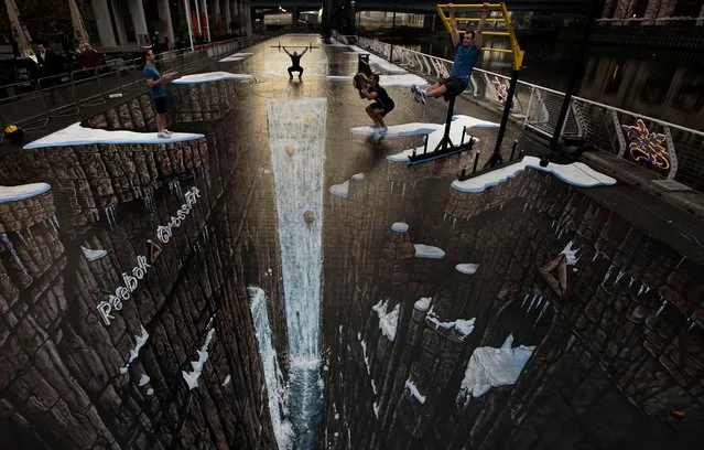 People break a world record as they take part in the world's largest and longest 3D anamorphic street painting, which is 198.36 feet long with a surface area of 9601 square feet, by British artist Joe Hill in the Canary Wharf district of London, November 17, 2011. (Photo by Matt Dunham/Associated Press)