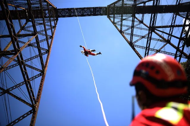 The Senior Officer of the Municipal Firefighters, Hector Chacon, dressed as Santa Claus, rappels down from a bridge, in Guatemala City, Guatemala, 17 December 2022. With joy and smiles, hundreds of children from three marginalized settlements in the northeast of Guatemala City received a visit on 17 December from a Santa Claus who comes down from a bridge every year and does not forget his gifts. This is the 76-year-old firefighter Hector Chacon, who started the tradition in 1997 and on 17 December again went down a bridge with the technique of rappelling to share gifts with children who live under scarce resources. (Photo by Edwin Bercian/EPA/EFE)