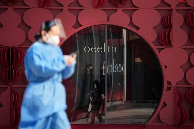 A woman in a protective suit walks past a shop, as coronavirus disease (COVID-19) outbreaks continue in Shanghai, China on December 19, 2022. (Photo by Aly Song/Reuters)