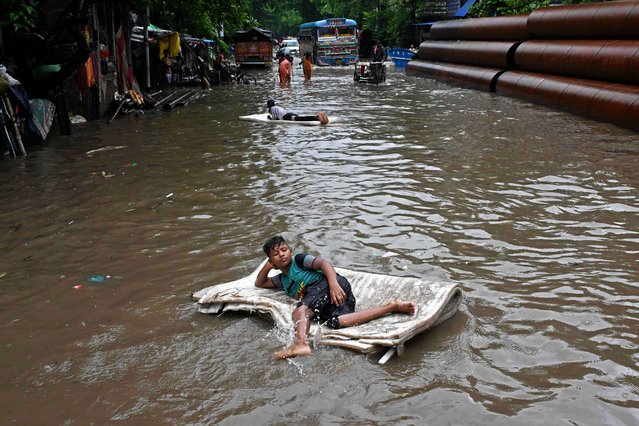 Children use foam sheets to float in a waterlogged street after heavy monsoon showers in Kolkata on July 8, 2025. India's annual monsoon season from June to September offers respite from the intense summer heat and is crucial for replenishing water supplies, but also brings widespread death and destruction. (Photo by Dibyangshu Sarkar/AFP Photo)