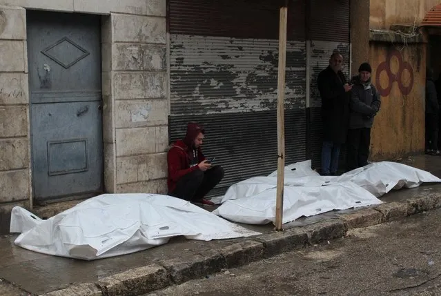 A man sits next to dead bodies in bags that lie on the floor, following an earthquake, in Aleppo, Syria on February 6, 2023. (Photo by Firas Makdesi/Reuters)
