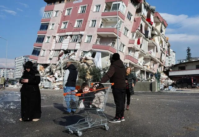 Children sit in a shopping cart near a collapsed building following an earthquake in Hatay, Turkey on February 7, 2023. (Photo by Umit Bektas/Reuters)