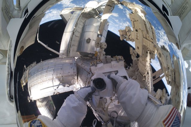 NASA spacewalker Mike Fossum's helmet visor mirrors a panoramic scene of the docked International Space Station with the space shuttle Atlantis and the blue and white Earth below, on July 12, 2011, in this NASA handout image. (Photo by Reuters/NASA)
