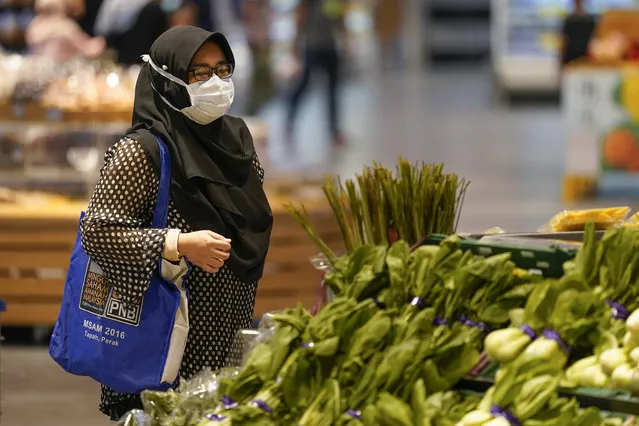 A shopper wearing a face mask to help curb the spread of the coronavirus looks at produce and a grocery in Putrajaya, Malaysia, Monday, October 5, 2020. Prime Minister Muhyiddin Yassin says he will self-quarantine after a Cabinet minister he was in contact with tested positive for the coronavirus. (Photo by Vincent Thian/AP Photo)