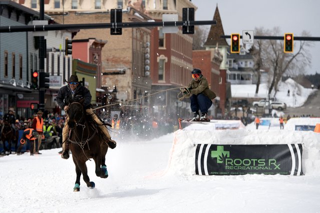 Rider Carl Gomez races down Harrison Avenue as skier Ben Southworth airs out a jump during the 75th annual Leadville Ski Joring weekend competition in Leadville, Colorado on March 4, 2023. Skijoring, which has its origins as a competitive sport in Scandinavia, has been adapted over the years to include a team made up of a rider and skier who must navigate jumps, slalom gates, and the spearing of rings for points. Leadville, with an elevation of 10,152 feet (3,094 m), the highest incorporated city in North America, has been hosting skijoring competitions since 1949. (Photo by Jason Connolly/AFP Photo)
