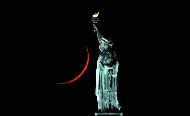 The moon sets behind the Statue of Liberty on November 16, 2020 in New York City. (Photo by Gary Hershorn/Getty Images)