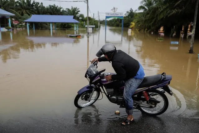 A man pushes his motorcycle in a flooded area in Yong Peng, Johor, Malaysia on March 4, 2023. (Photo by Hasnoor Hussain/Reuters)