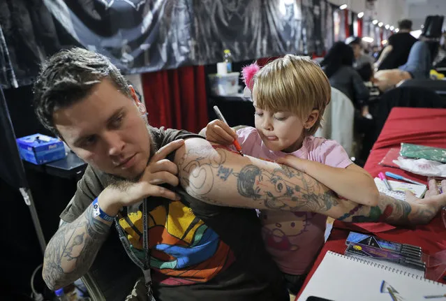 Ave, 4 years-old, of the United States, paints on her father's hand during the International Tattoo Convention Bucharest 2016 in Bucharest, Romania, Sunday, October 16, 2016. (Photo by Vadim Ghirda/AP Photo)