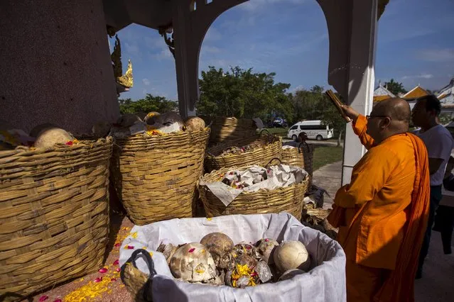 A buddhist monk sprays holy water on skulls and skeletons of unclaimed bodies during a buddhist ceremony at the Poh Teck Tung Foundation Cemetery in Samut Sakhon province, Thailand, November 11, 2015. (Photo by Athit Perawongmetha/Reuters)