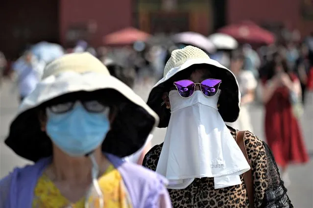 A woman shelters under a mask as she walks out of the Forbidden City during hot weather conditions in Beijing on June 16, 2023. (Photo by Wang Zhao/AFP Photo)