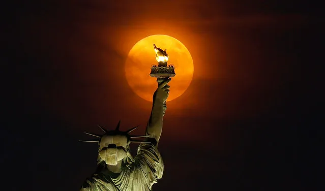 A 99.7 percent illuminated Buck Moon rises through a haze behind the Statue of Liberty in New York City on July 2, 2023, as seen from Jersey City, New Jersey. (Photo by Gary Hershorn/Getty Images)