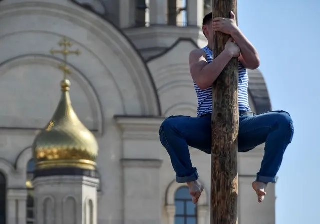 A man climbs up a wooden pole to get a prize in front of an Orthodox cathedral during celebrations of Maslenitsa, also known as Pancake Week, which is a pagan holiday marking the end of winter, in Russia's far eastern city of Vladivostok, Russia on March 14, 2021. (Photo by Yuri Maltsev/Reuters)