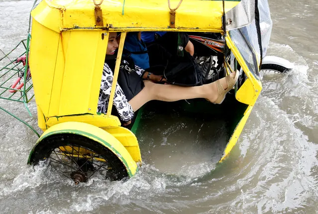 A commuter raises her feet to stay dry as she rides a pedicab, a pedaled tricycle, to go to work amidst flooding in a street in Manila, Philippines, after overnight Southwest monsoon rains brought about by tropical storm Ampil inundated low-lying areas in Metropolitan Manila and nearby provinces Friday, July 20, 2018. (Photo by Bullit Marquez/AP Photo)