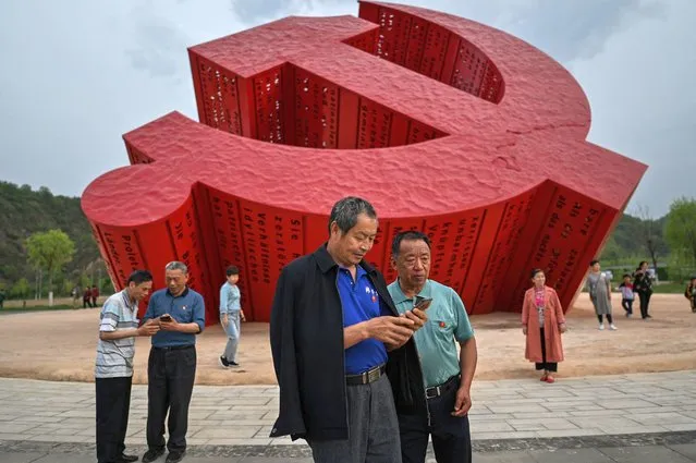 This picture taken during a government organised media tour shows people looking at the photos they took next to a monument of the hammer and sickle in Nanniwan, some 60 kms from Yan'an, the headquarters of the Chinese Communist Party from 1936 to 1947, in Shaanxi province on May 11, 2021, ahead of the 100th year of the party's founding in July. (Photo by Hector Retamal/AFP Photo)
