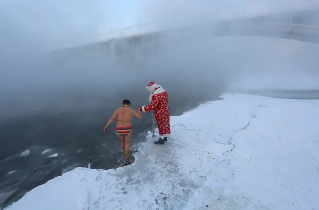 A man dressed as Ded Moroz, the Russian equivalent of Santa Claus, helps a member of the Cryophile amateur winter swimmers' club, who walks into the icy waters of the Yenisei River during an event marking the New Year and Christmas season, with the air temperature at about minus 26 degrees Celsius (minus 14.8 degrees Fahrenheit), in Krasnoyarsk, Russia December 30, 2018. (Photo by Ilya Naymushin/Reuters)