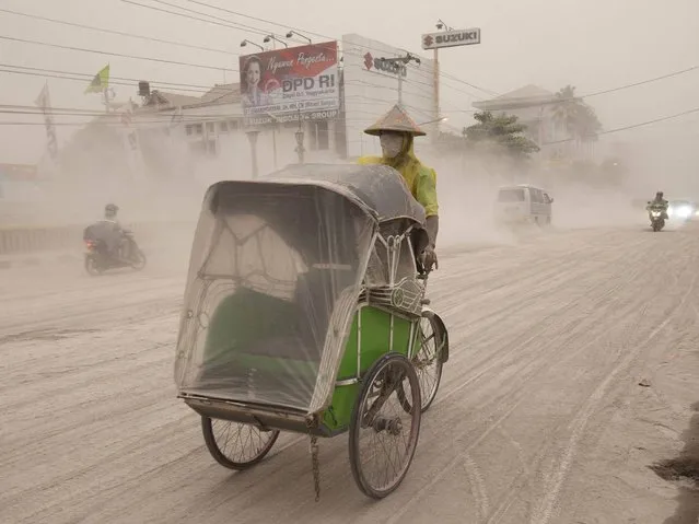 A man wears a mask as he rides a becak, a kind of rickshaw, on a road covered with from Mount Kelud in Yogyakarta. (Photo by Dwi Oblo/Reuters)