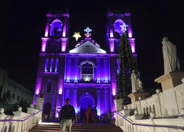 People walk past an illuminated St. Joseph Cathedral on the eve of the Christmas, in Hyderabad, India, Friday, December 24, 2021. (Photo by Mahesh Kumar A./AP Photo)