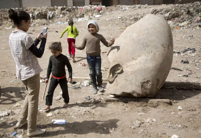 A child poses for a picture past a recently discovered statue in a Cairo slum that may be of pharaoh Ramses II, in Cairo, Egypt, Friday, March 10, 2017. Archeologists in Egypt have discovered a massive statue that may be of pharaoh Ramses II, one of the country 's most famous ancient rulers. The colossus, whose head was pulled from mud and groundwater by a bulldozer on Thursday, is around eight meters (yards) tall and was discovered by a German-Egyptian team. (Photo by Amr Nabil/AP Photo)