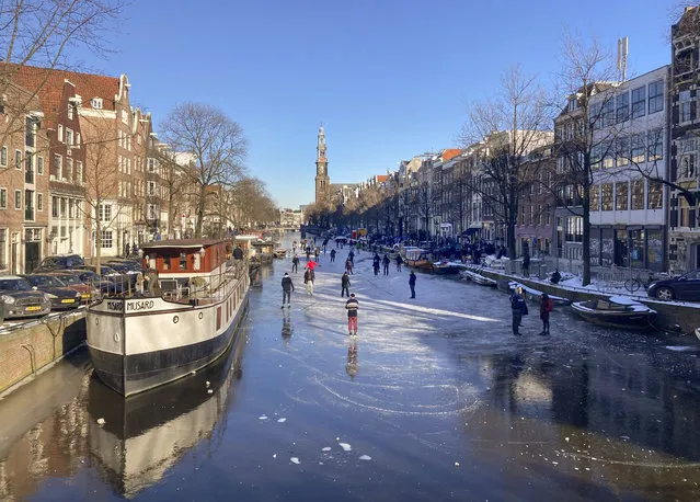 Dozens of skaters took to the frozen surface of Amsterdam's historic Prinsengracht canal in Amsterdam, Netherlands, Saturday, February 13, 2021, as the deep freeze gripping Europe briefly made it possible to skate on a small section of the canal for the first time since 2018. People skated and walked on a small stretch of ice between two bridges close to the landmark Westerkerk before growing cracks in the ice forced all but the most daring off the ice. in Amsterdam, Netherlands, Saturday, Feb. 13, 2021. (Photo by Mike Corder/AP Photo)