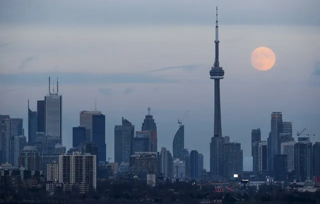 The moon rises behind the CN Tower, a Canadian landmark, and the skyline in Toronto, Canada November 24, 2015. (Photo by Mark Blinch/Reuters)
