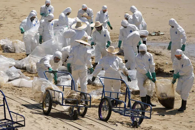 Workers carry out a cleanup operation on Mae Ramphueng Beach after a pipeline oil spill off the coast of Rayong province in eastern Thailand, Sunday, January 30, 2022. The governor of a province in eastern Thailand on Saturday declared a state of emergency after an oil slick washed up on a sand beach, shutting down restaurants and shops in a setback for the pandemic-hit tourism industry. (Photo by Sakchai Lalit/AP Photo)