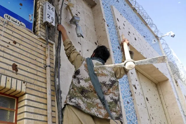An Afghan protester hits the building of Iranian consulate with a pickaxe during a demonstration against the alleged published reports of harassment of Afghan refugees in Iran, in Herat on April 11, 2022. (Photo by Mohsen Karimi/AFP Photo)