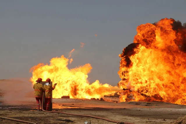Oil workers and firemen try to extinguish flames at the Khabbaz oil field some 20 kilometres southwest of Kirkuk on June 1, 2016 following a reported improvised explosive attack by the Islamic State (IS) group. The Khabbaz oil field produces around 20,000 barrels of oil per day and is situated between areas disputed by opposing fighters from the Iraqi Kurdish Peshmerga forces and the Islamic State (IS) group. (Photo by Marwan Ibrahim/AFP Photo)