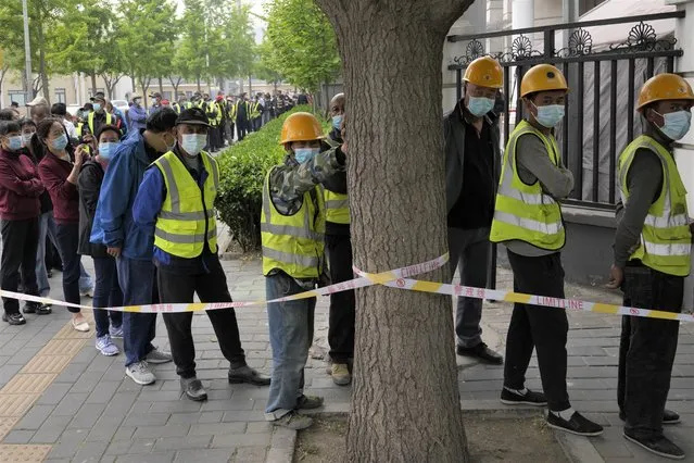 Workers wearing masks line up for mass COVID testing in Chaoyang District on Monday, April 25, 2022, in Beijing. (Photo by Ng Han Guan/AP Photo)