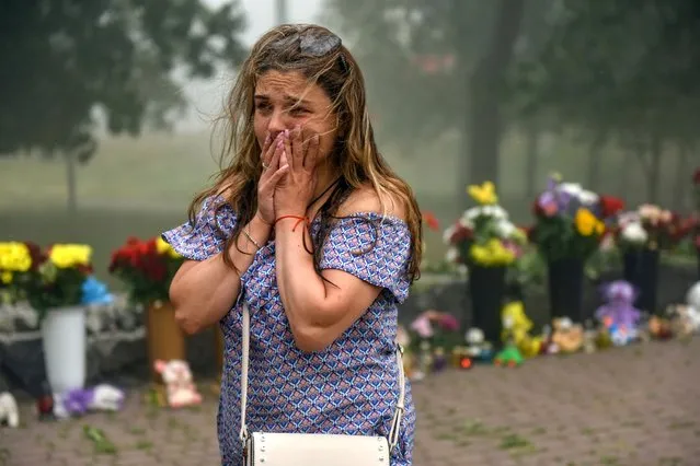 A woman cries near the flowers, brought to  the destroyed Amstor shopping mall in Kremenchuk, Ukraine, 28 June 2022. At least 18 people died following Russian airstrikes on the crowded shopping mall, the State Emergency Service (SES) of Ukraine said in a Telegram post. The Amstor shopping center one-story building was hit by Russian rockets on 27 June afternoon. (Photo by Oleg Petrasyuk/EPA/EFE)